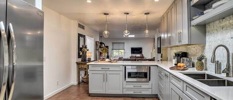 A modern kitchen with a central island, stainless steel appliances, pendant lighting, and a tiled backsplash.