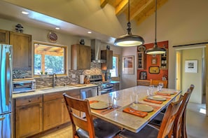A modern kitchen with wooden cabinets, a large island, and a dining area set for six. - Hidden Santa Fe Gem - Nestled in Tesuque Hills! (Santa Fe)