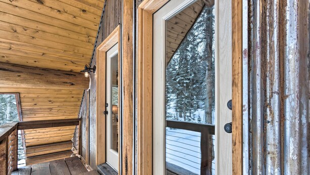 A wooden cabin with a porch, large windows, and a view of snow-covered trees.