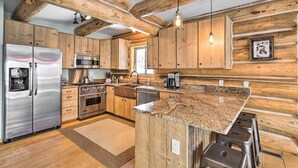 A modern kitchen with wooden cabinetry, stainless steel appliances, granite countertops, and a hanging light fixture.
