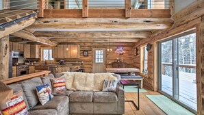 A log cabin interior with a cozy living area, a kitchen, and large windows.