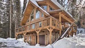 A wooden cabin with a balcony, large windows, and a staircase leading to the upper level.