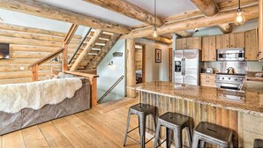 A rustic kitchen with wooden beams, a stone island, bar stools, and modern appliances.