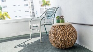 Un balcón con una mesa redonda de mimbre, una silla de metal y una pequeña planta en maceta.