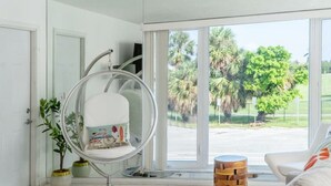 Una habitación moderna con un ventanal grande, una silla colgante, una mesita pequeña y una planta en maceta.