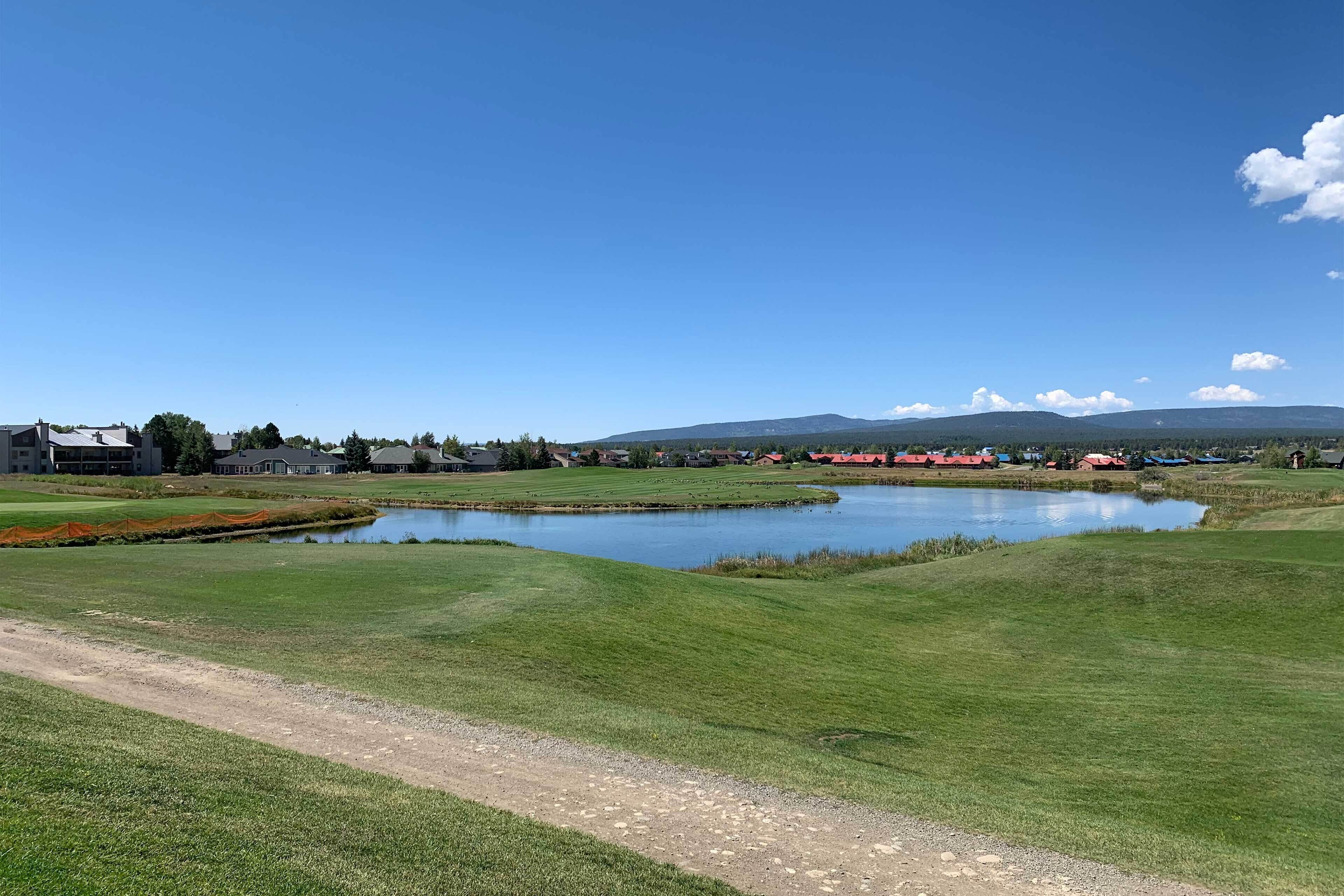 A golf course with a pond, houses, and a mountain in the background.