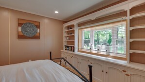 Een slaapkamer met een bed, inbouwschappen, een raam met zonwering en een decoratief wandobject.