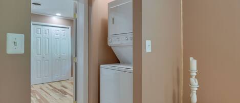 Une buanderie équipée d’un lave-linge et d’un sèche-linge, d’une commode en bois et, au fond, d’une porte blanche.