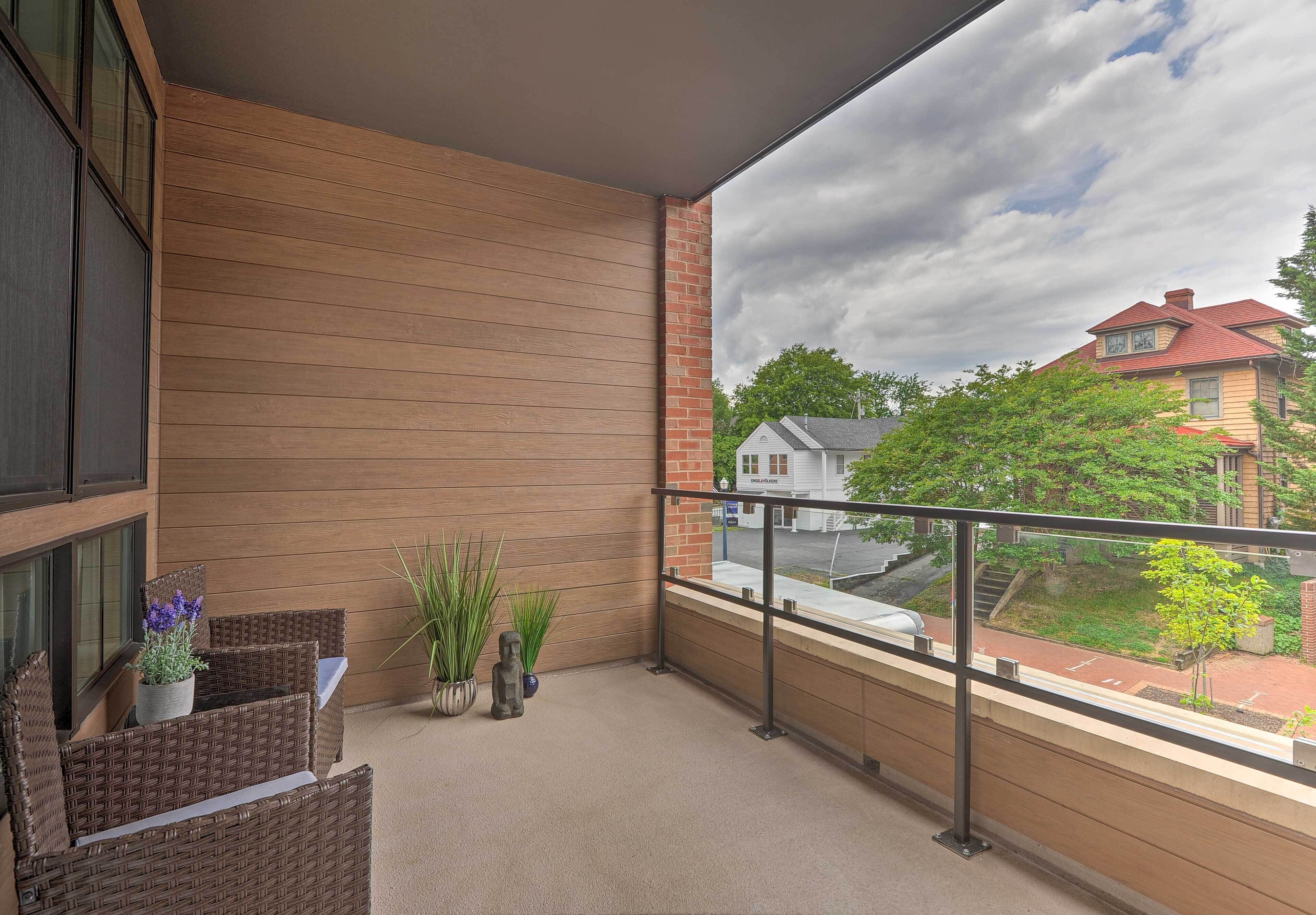 A balcony with wicker furniture, potted plants, and a view of a residential area.