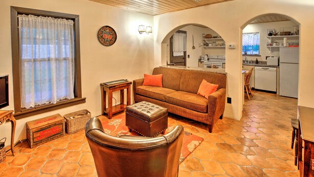 A cozy living room with a leather armchair, a brown sofa, and a wooden coffee table. There is a kitchen visible through an archway. - Charming Couples Casita, Walk to Old Mesilla Plaza (Mesilla)
