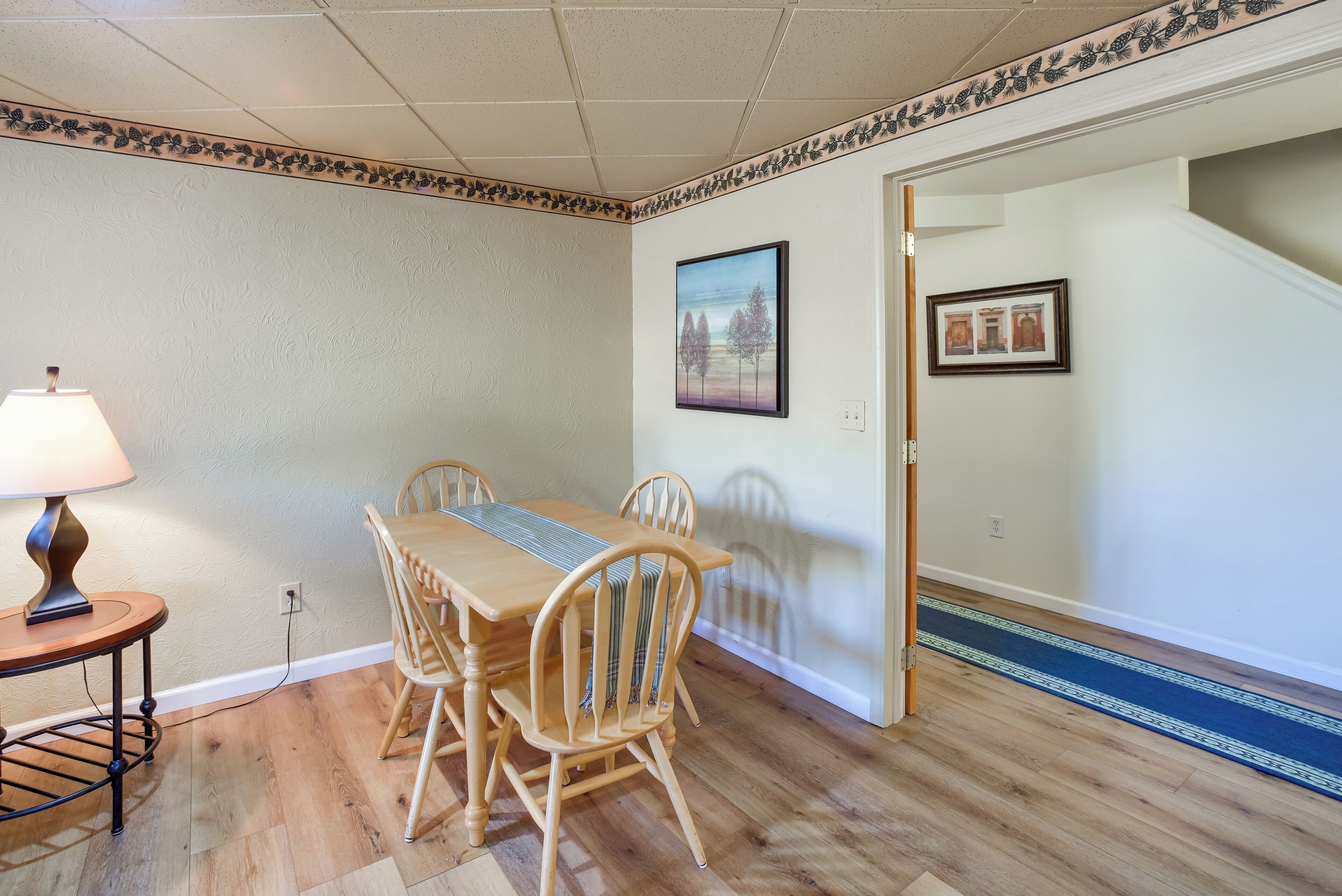 A dining area with a wooden table and chairs, a lamp, and a patterned border on the ceiling.