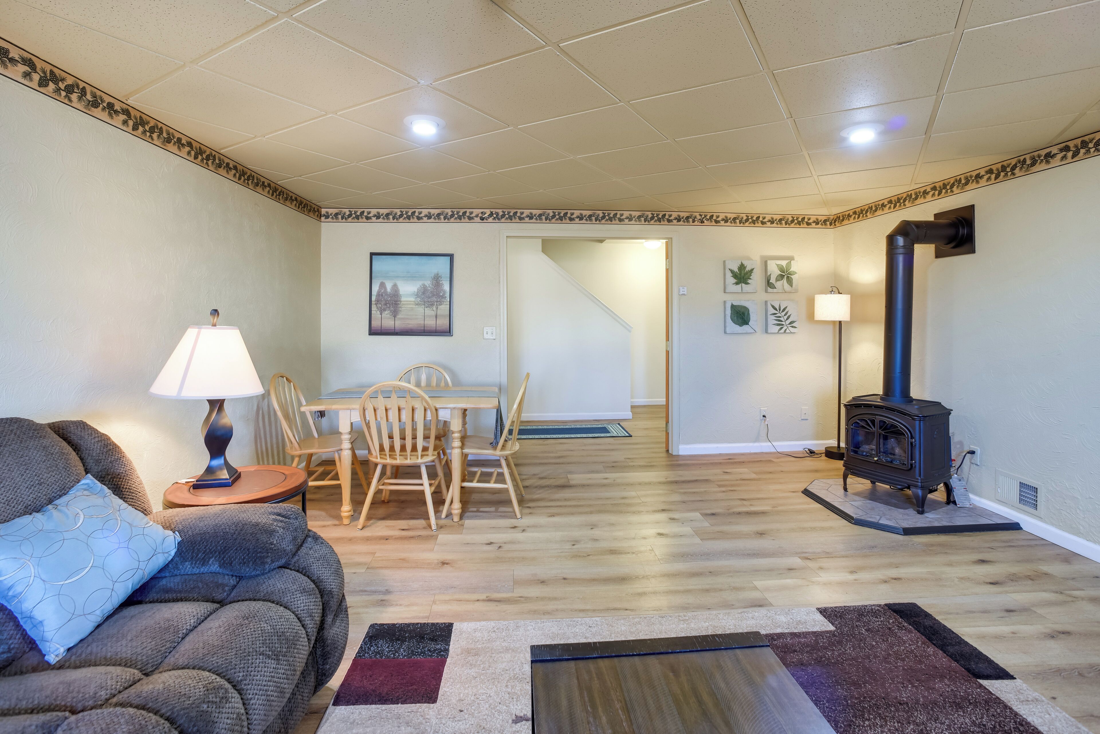Una sala de estar con un sofá, una lámpara, una mesa de comedor con sillas, una chimenea y una escalera que lleva a otra habitación.