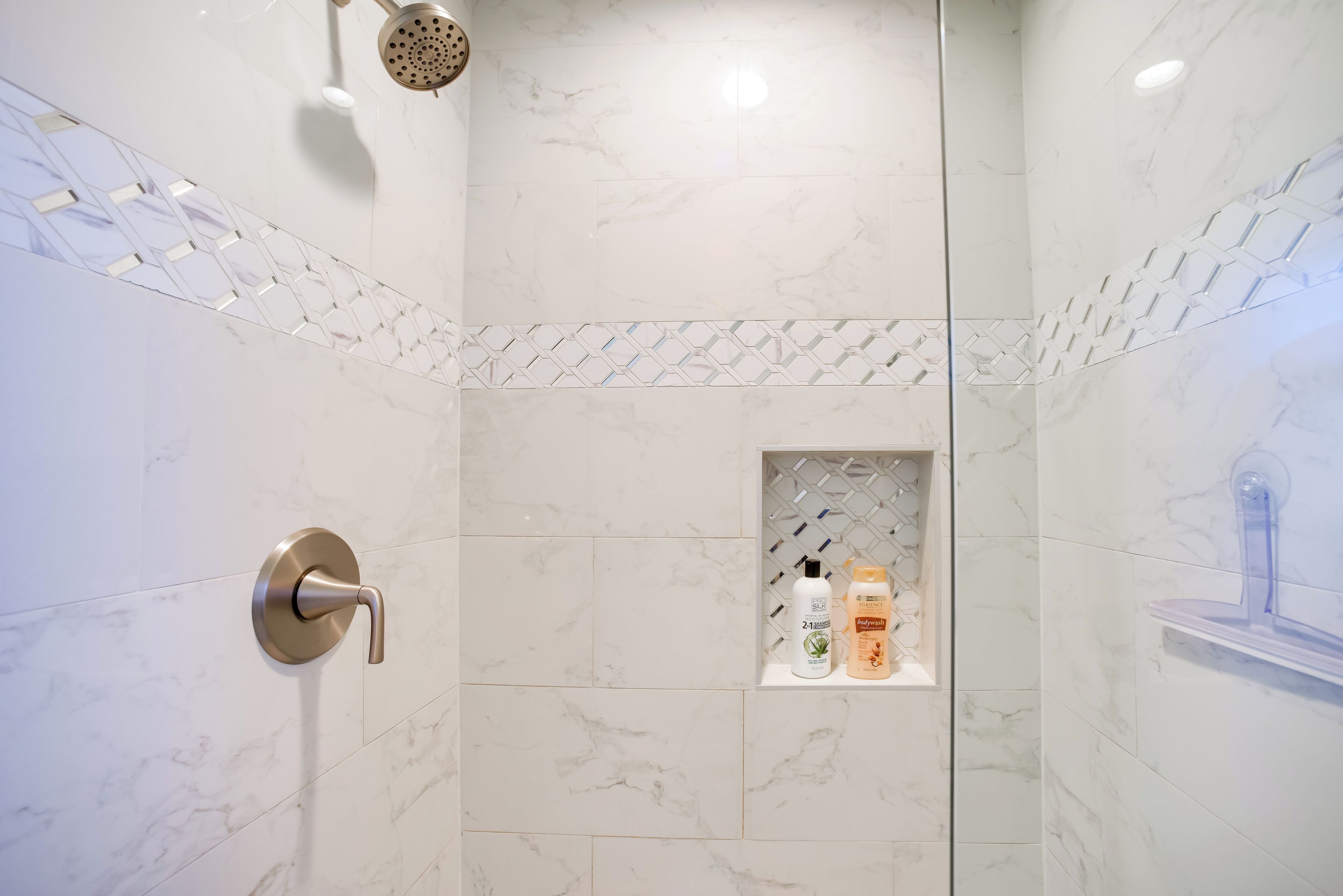 Ein modernes Badezimmer mit Dusche, Marmorfliesen, einer integrierten Ablagefläche für Toilettenartikel und einem Duschkopf.