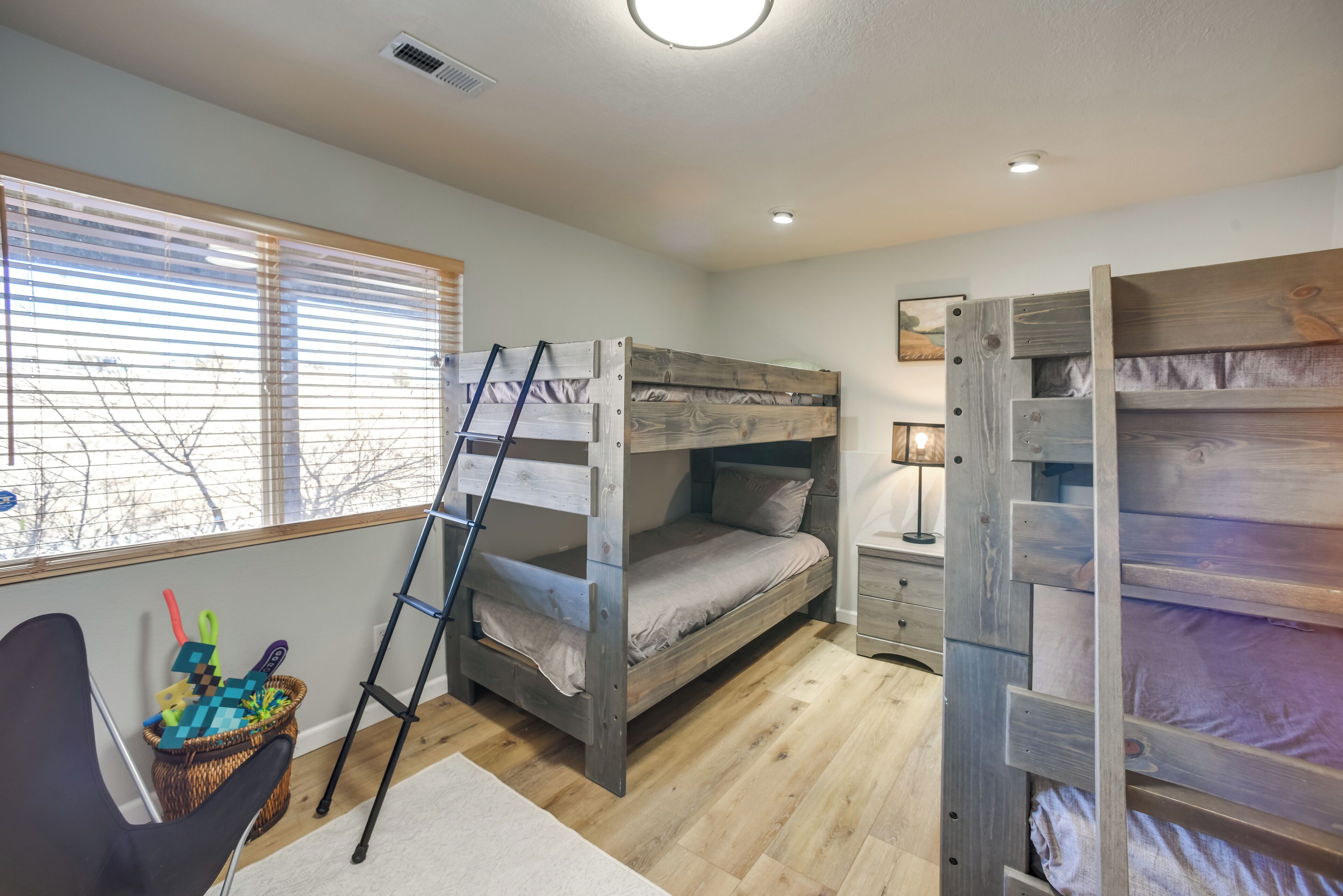 A room with bunk beds, a ladder, a desk, and a window with blinds.
