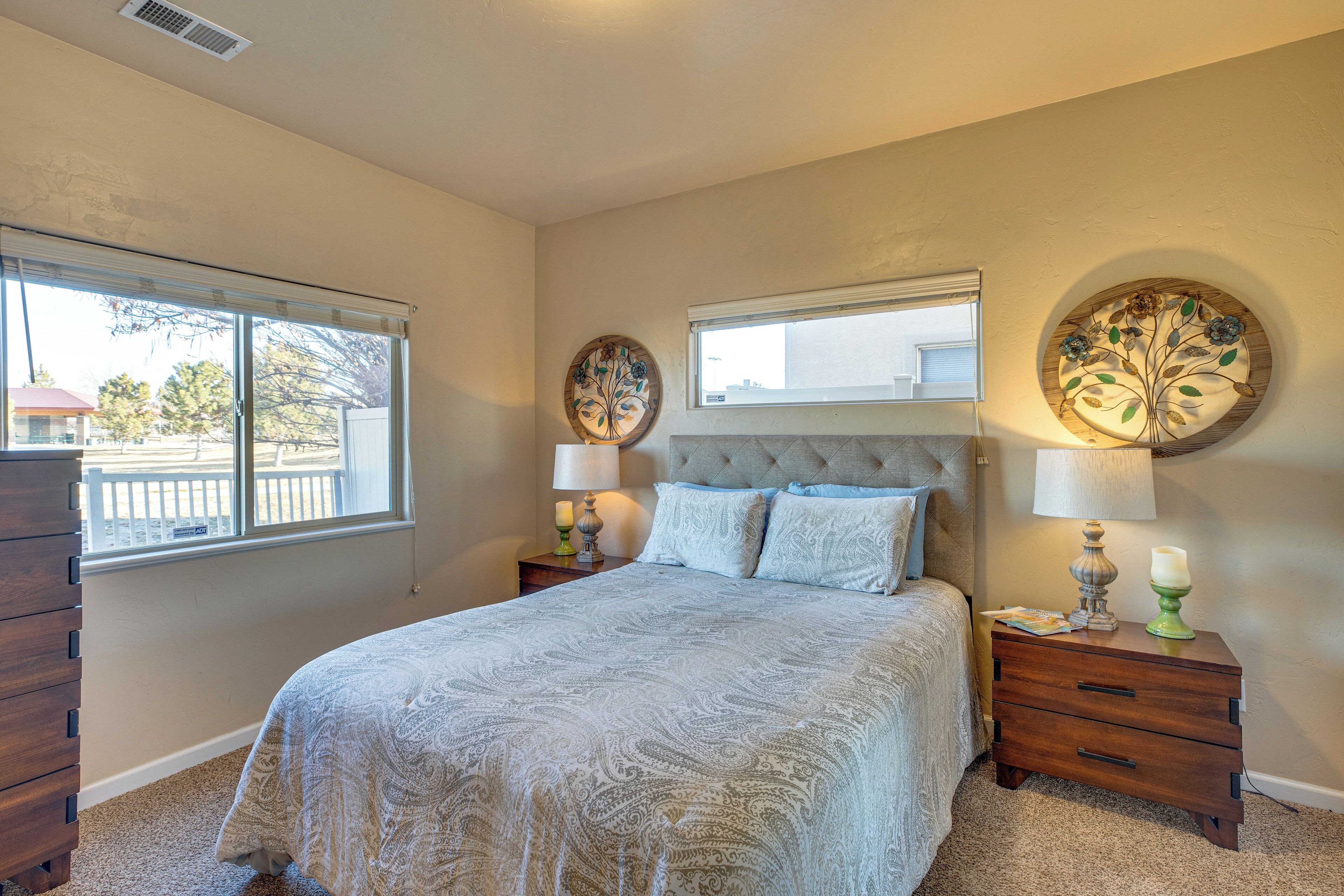 A bedroom with a large bed, two bedside tables with lamps, a dresser, and decorative wall art.