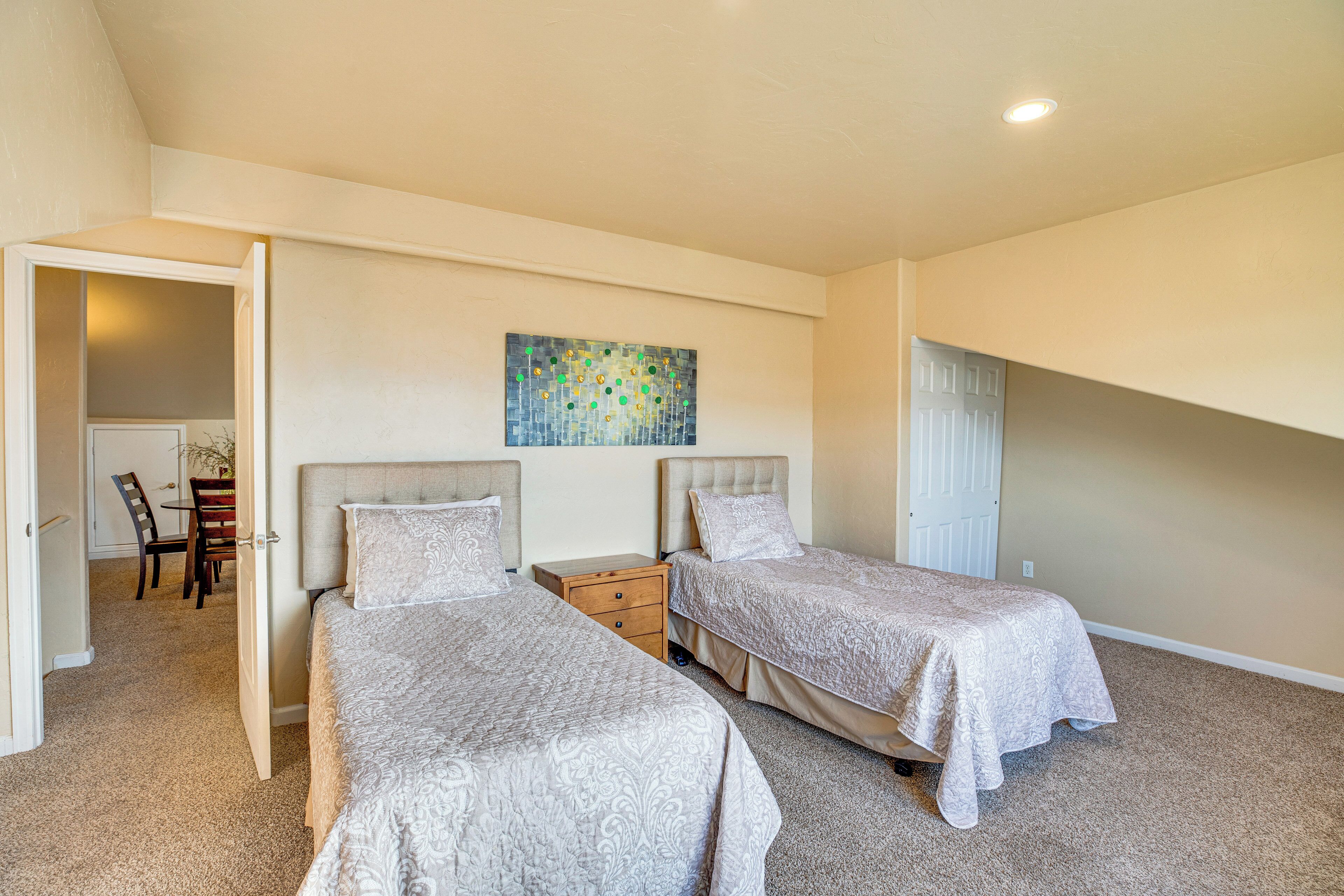 A bedroom with two beds, a small wooden nightstand, a dining table with chairs, and a colorful abstract painting on the wall.