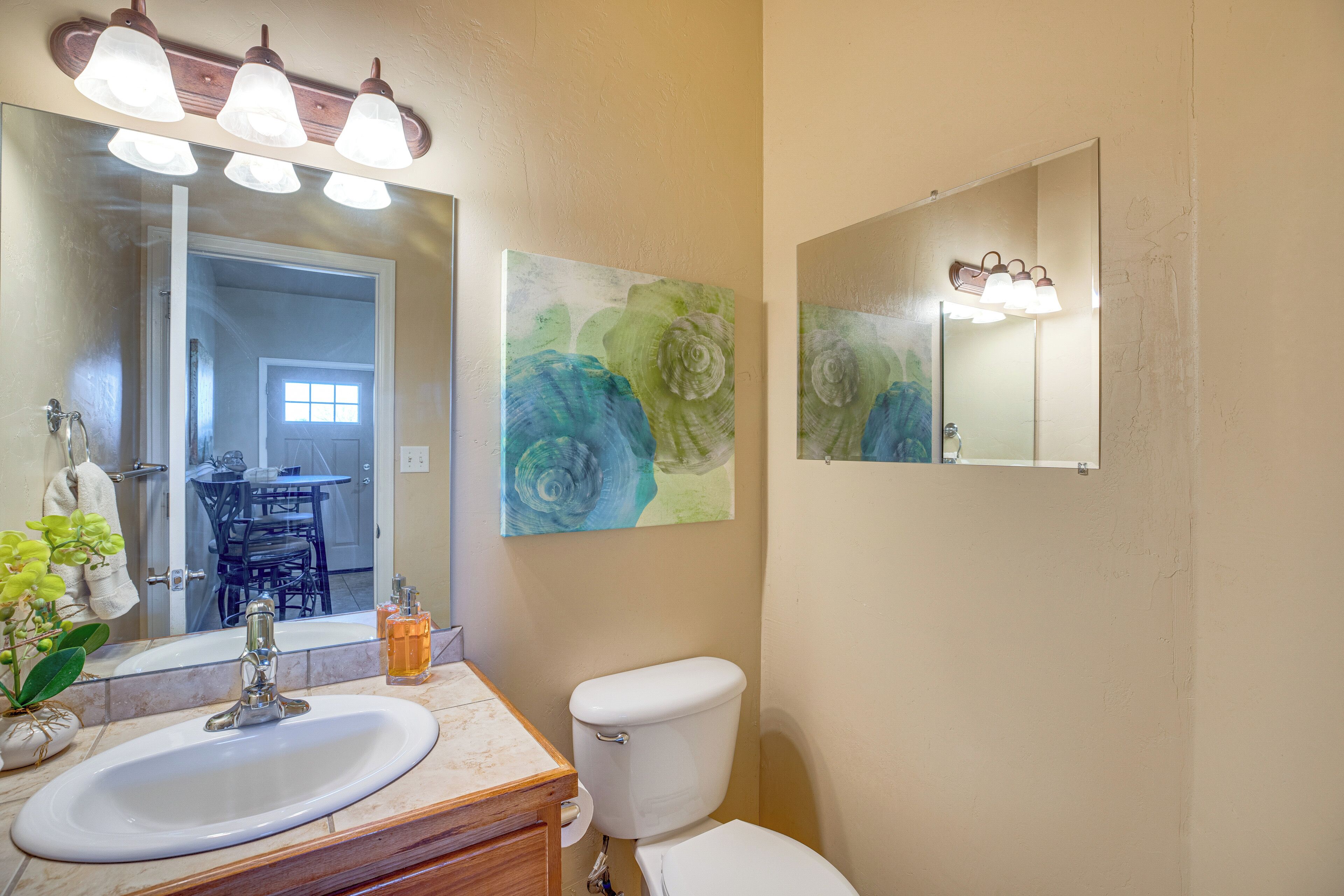 A bathroom with a sink, mirror, toilet, and two wall-mounted light fixtures.