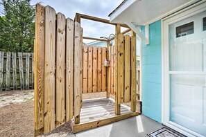 Um deck de madeira com área de chuveiro integrada, uma porta branca e uma parede externa azul.