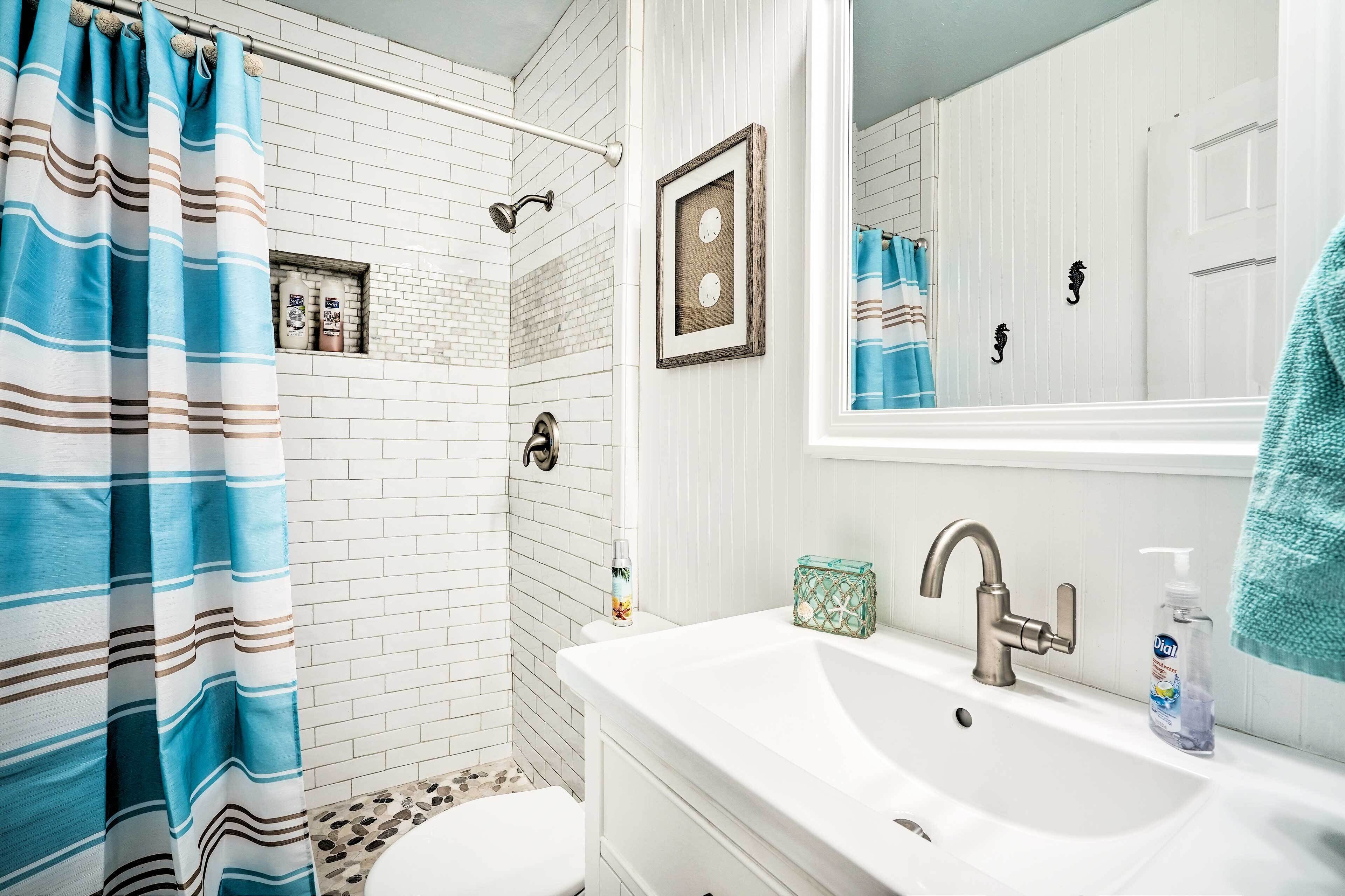 A bathroom with a shower, toilet, sink, and a mirror.