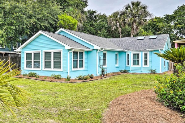 Uma casa de dois andares com fachada azul, telhado inclinado e um jardim da frente com gramado e um canteiro pequeno.