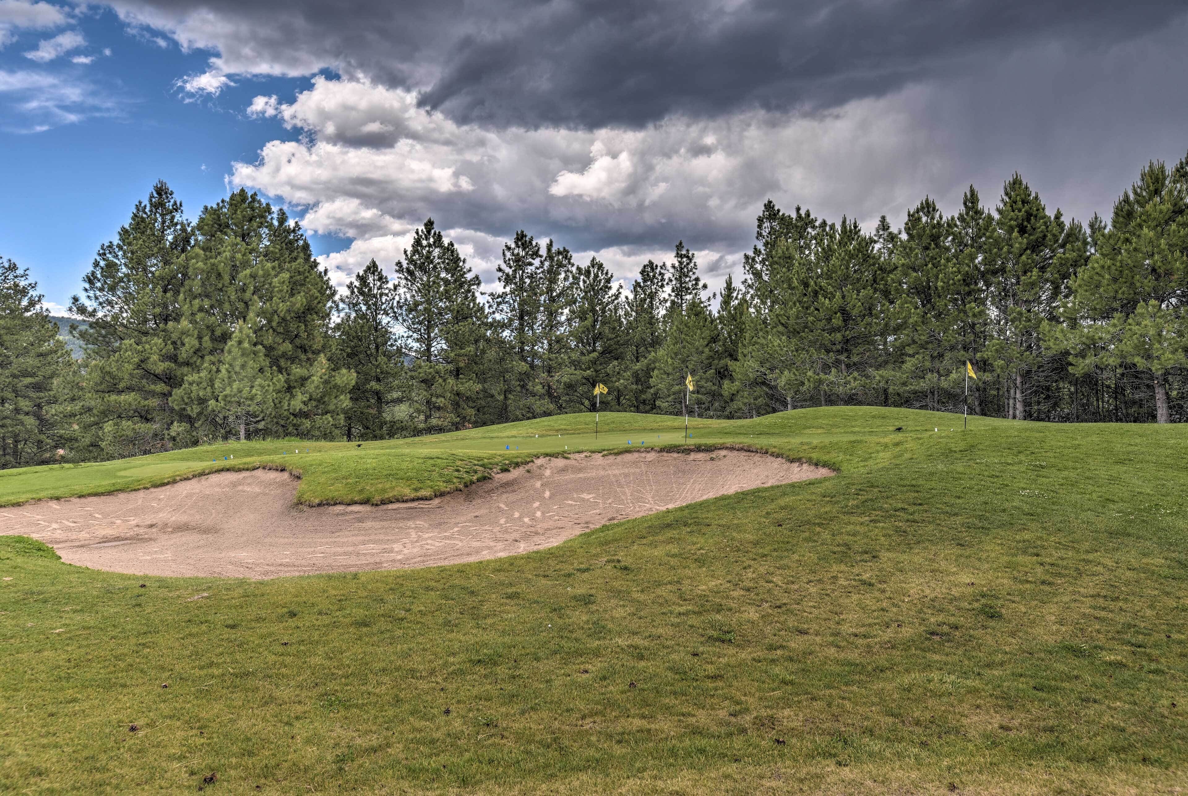 Un parcours de golf avec un bunker de sable, de l’herbe verte et une forêt en arrière-plan.