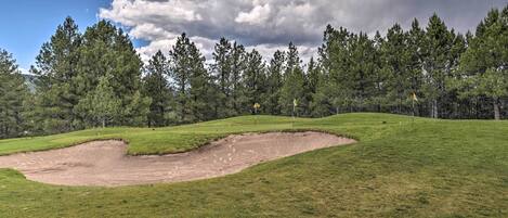 Un parcours de golf avec un bunker de sable, de l’herbe verte et une forêt en arrière-plan.