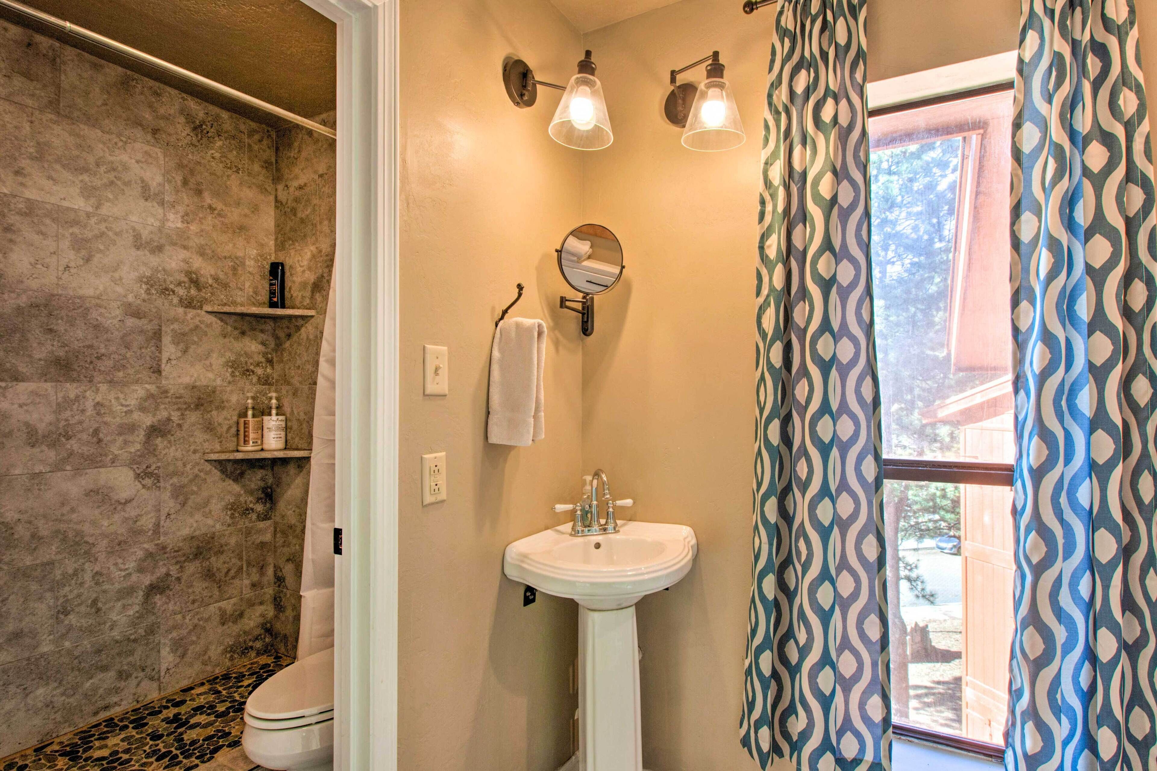 Un baño con pared de piedra, un lavamanos pedestal, un espejo y una ventana con cortinas estampadas.