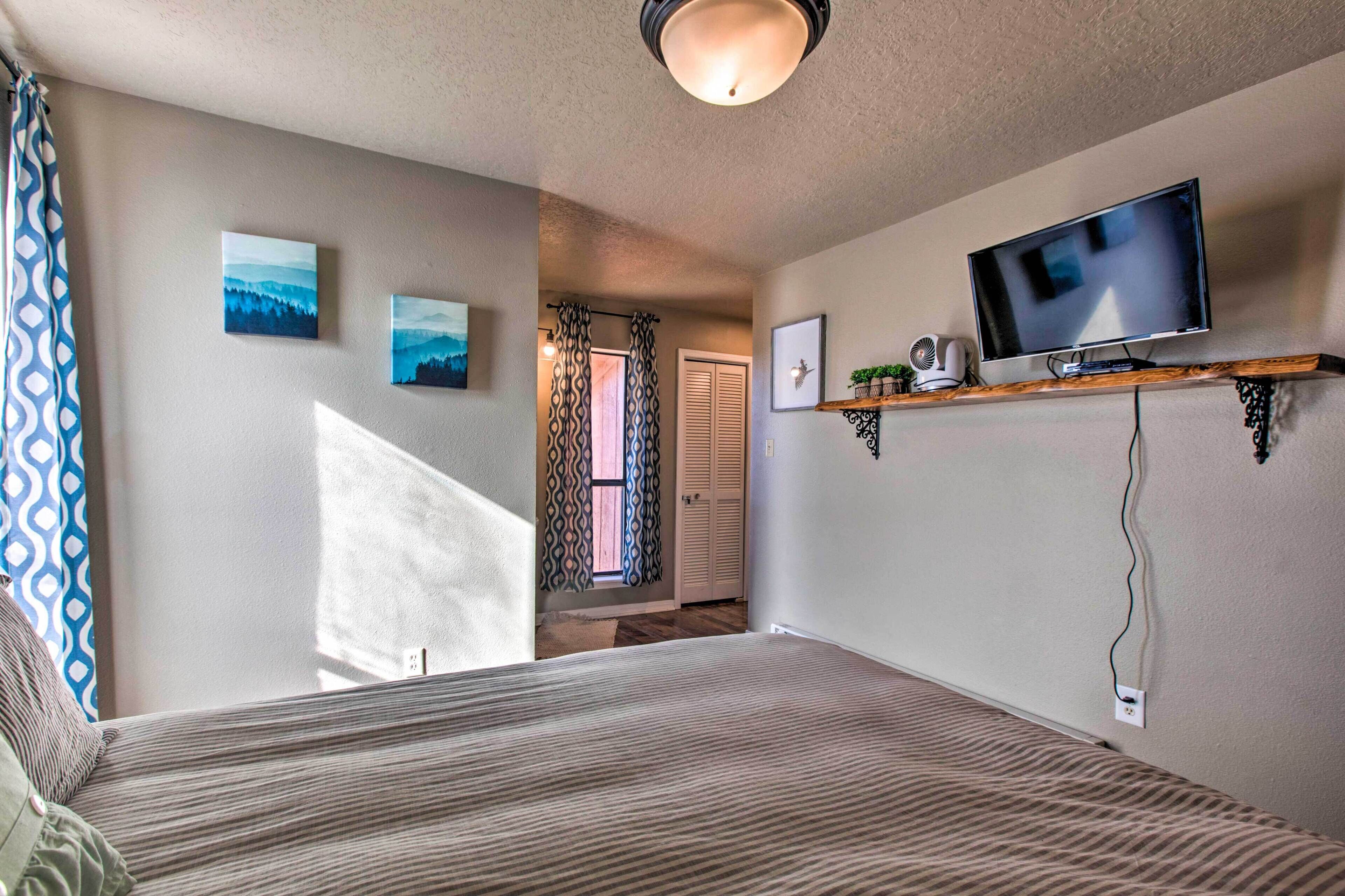 Un dormitorio con cama, televisor en un estante y ventana con cortinas.