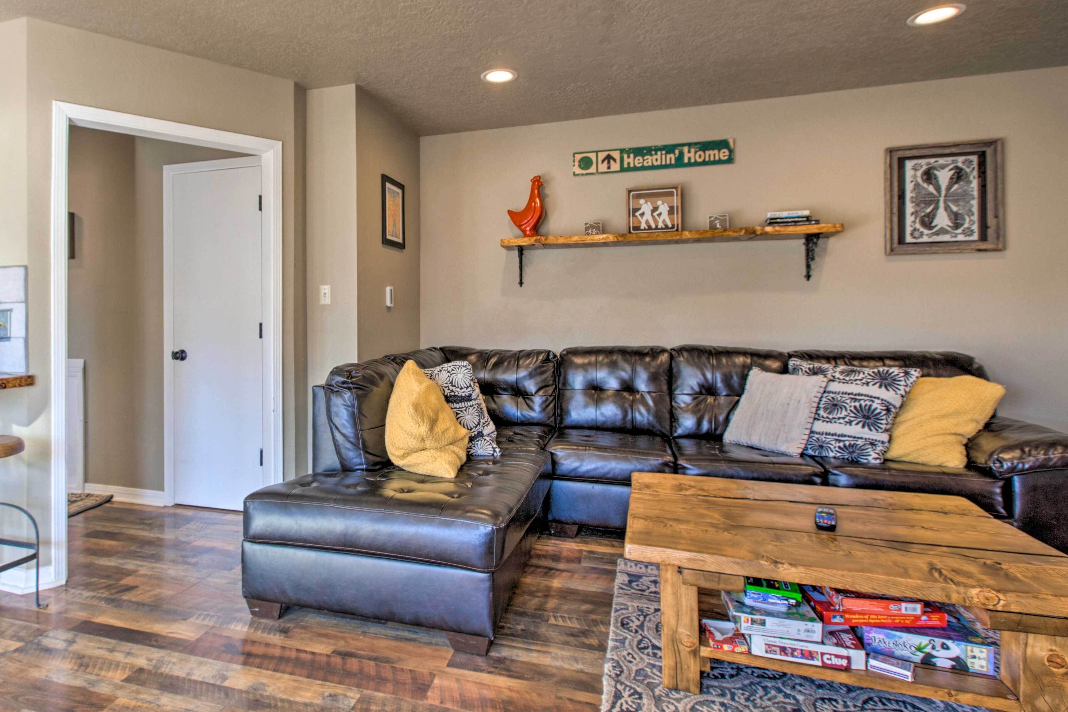 A living room with a leather sectional sofa, a wooden coffee table with board games, and a 'Headin' Home' sign on the wall.