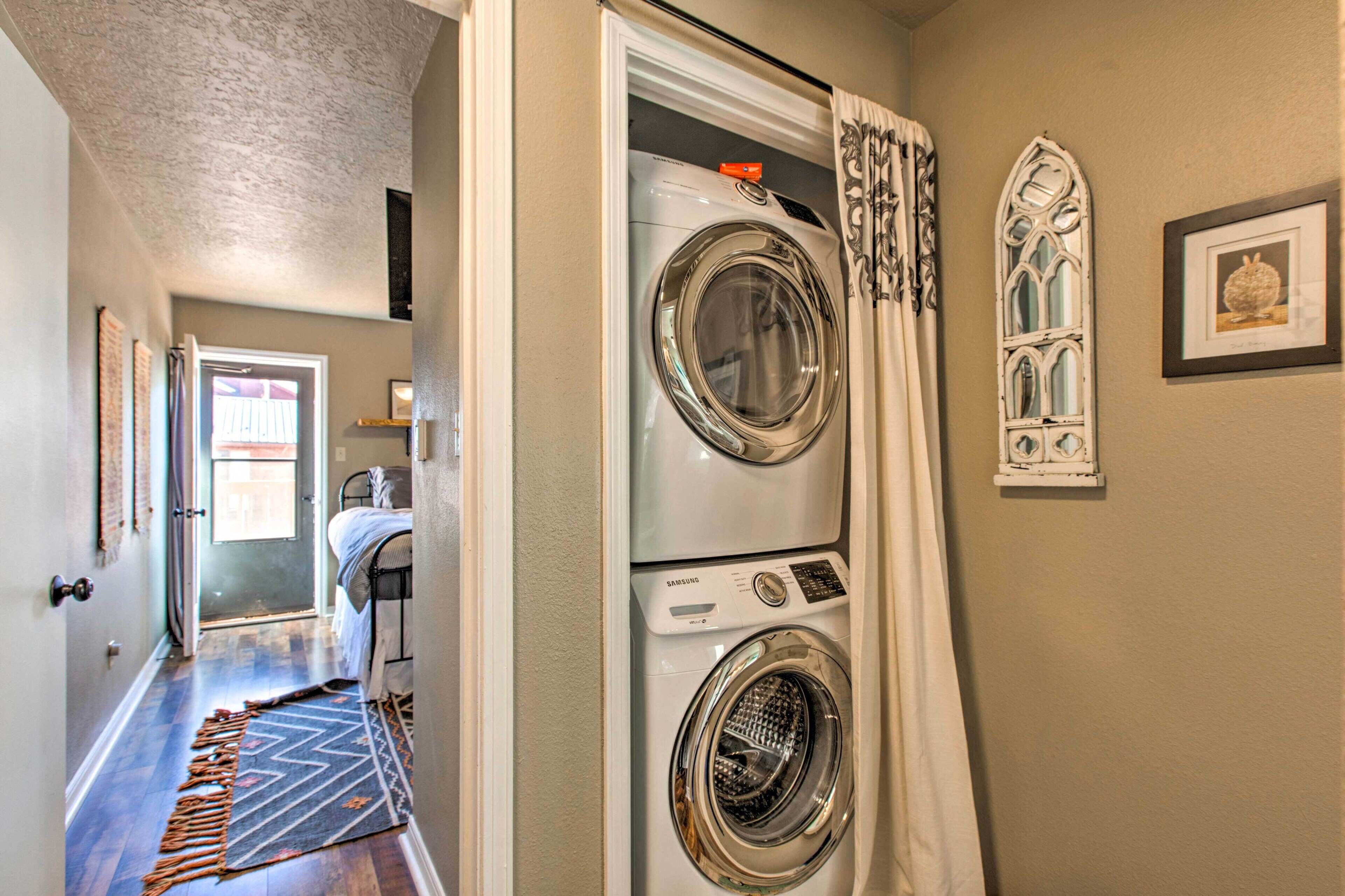 A laundry room with stacked washers and dryers, a patterned rug, and decorative wall art.