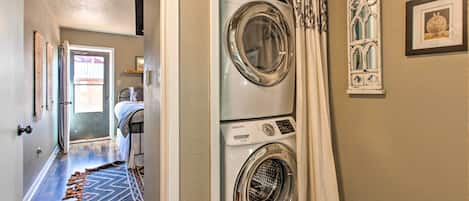 A laundry room with stacked washers and dryers, a patterned rug, and decorative wall art.