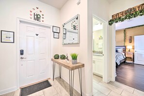A hallway with a white door, a console table with decorative items, a mirror with a heart-shaped decoration, and a bed in the adjacent room. - Davenport Retreat w/ Themed Rooms, Patio & Pool! (Davenport)