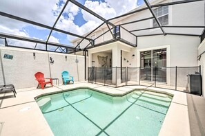 Et poolområde med en klar, blå pool, et overdækket siddeområde med Adirondack-stole og udsigt til en bygning med balkon.