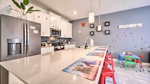 A modern kitchen with a stainless steel refrigerator, microwave, and coffee machine. There are white cabinets, a granite countertop, and a dining area with colorful chairs. - Davenport Retreat w/ Themed Rooms, Patio & Pool! (Davenport)