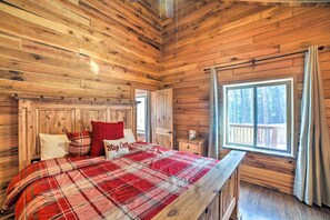 Een slaapkamer in een houten hutje, met een bed, nachtkastje en een raam met uitzicht op een terras.