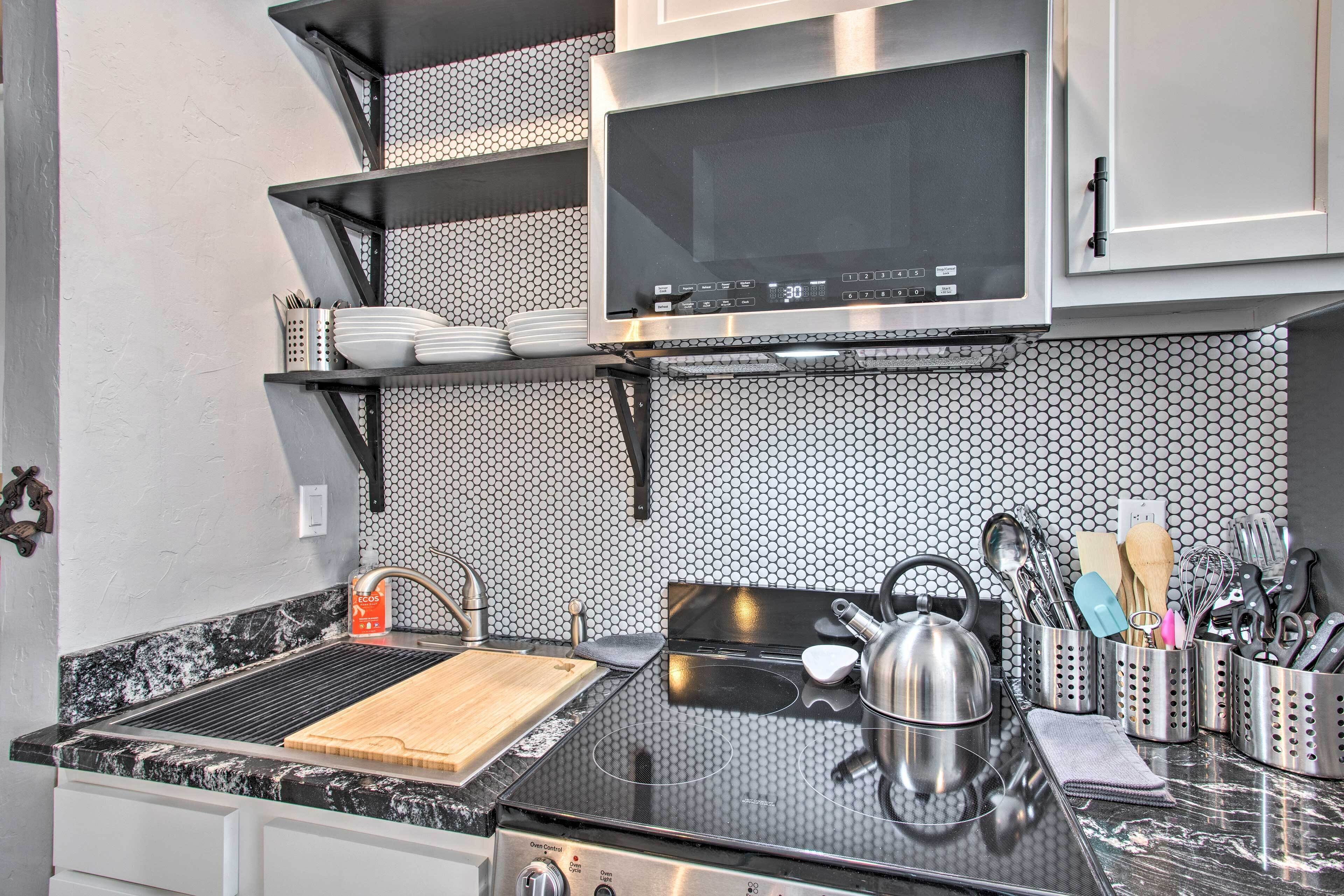 A kitchen with a black countertop, a kettle, and various utensils.