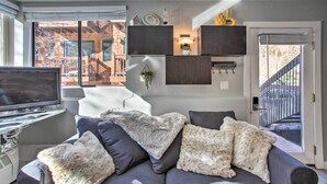 A modern living room with a grey sofa, a flat-screen TV, and a large window with a view of a building. - Telluride Studio in Downtown - Walk to Gondola! (Telluride)