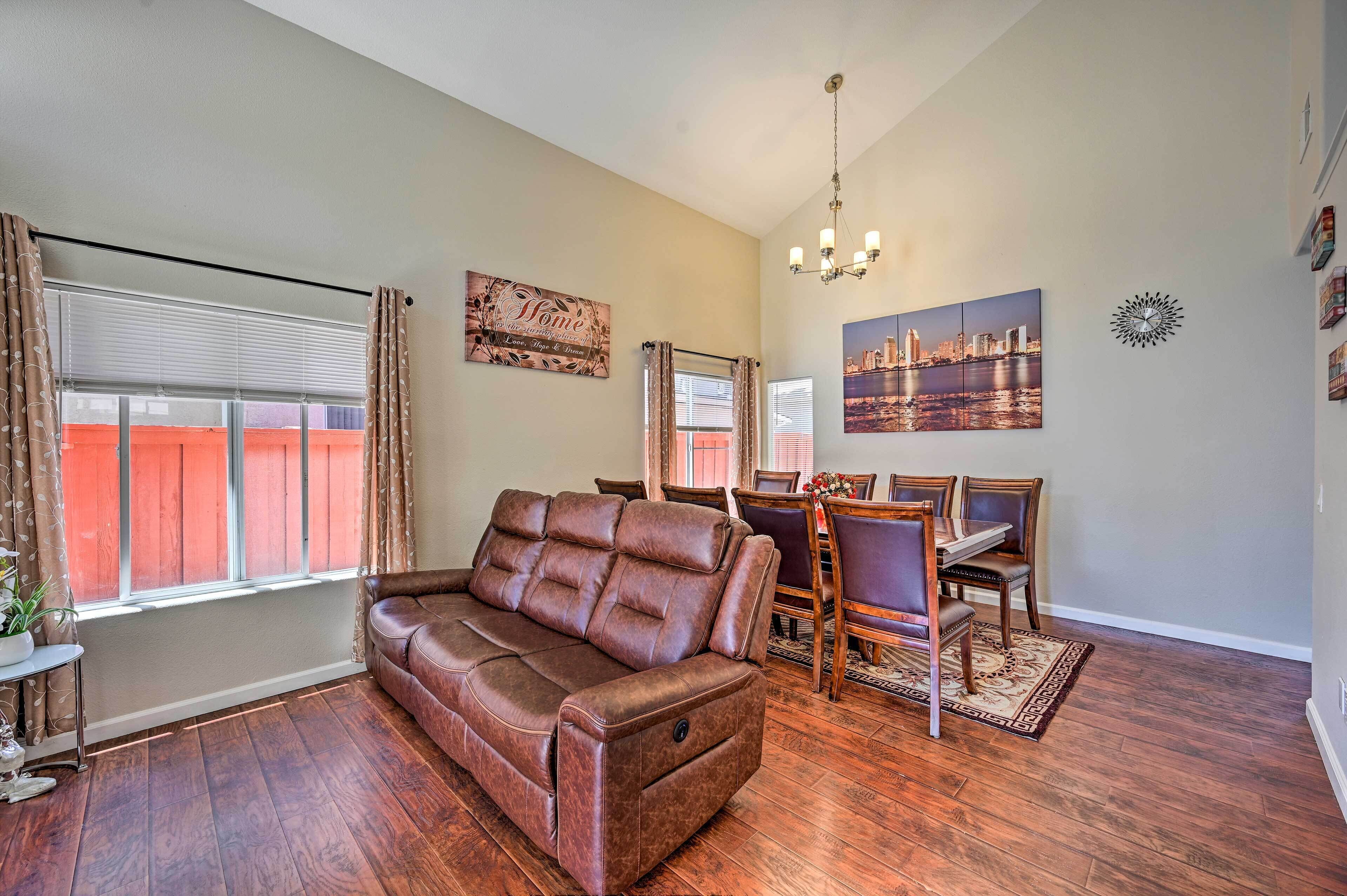 A living room with a brown leather sofa, dining table with chairs, and a cityscape painting on the wall.