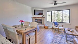 A modern living room with a fireplace, a dining table with chairs, a sofa, and a large window with a view of trees. - Frisco Mountain Hub: Walk to Main Street (Frisco)