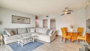 A living room with a sofa, coffee table, and dining area with chairs. - Direct Beach Access & View: Satellite Beach Condo! (Satellite Beach)