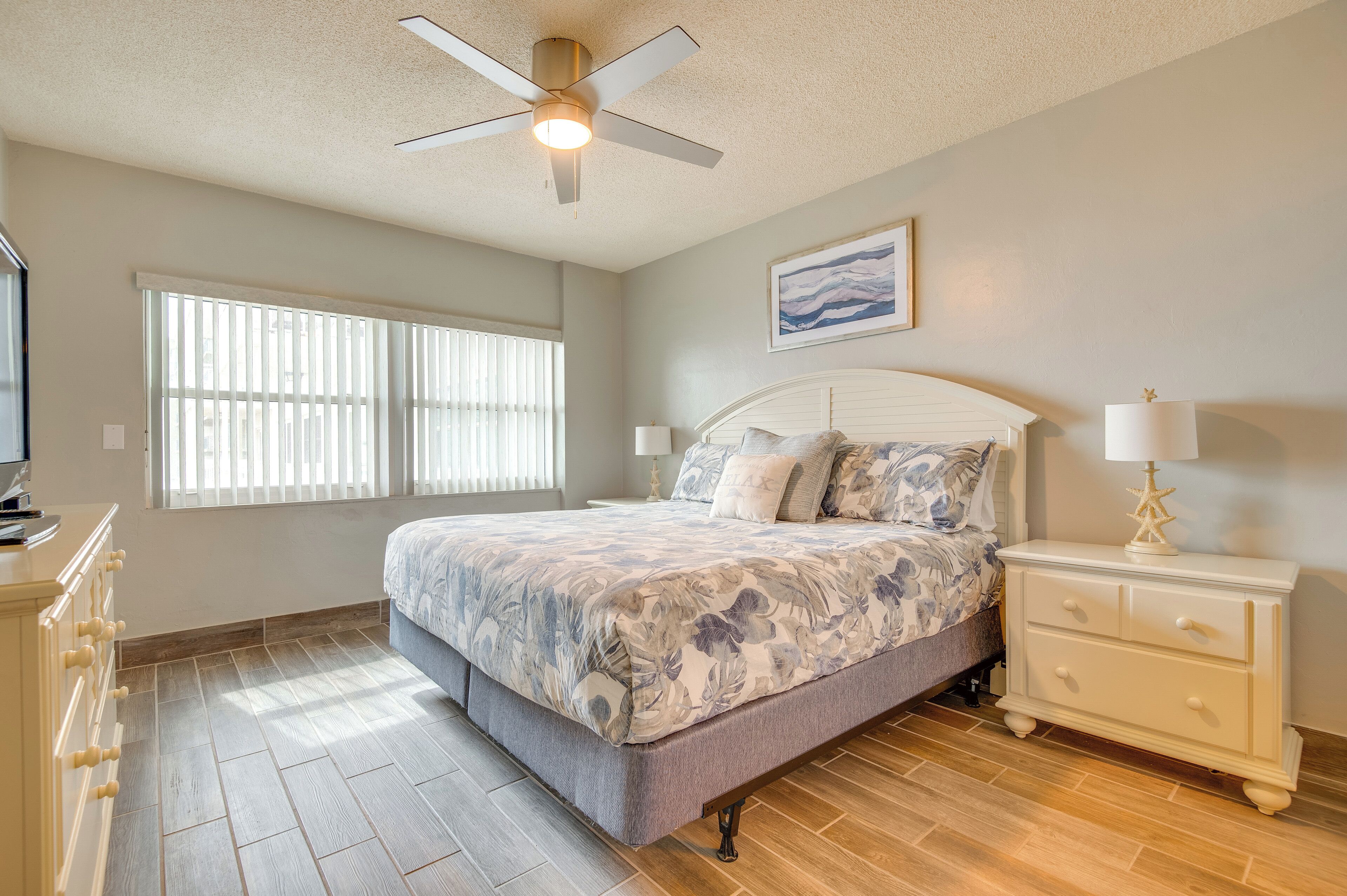 A bedroom with a bed, nightstands, a ceiling fan, and a window with blinds.