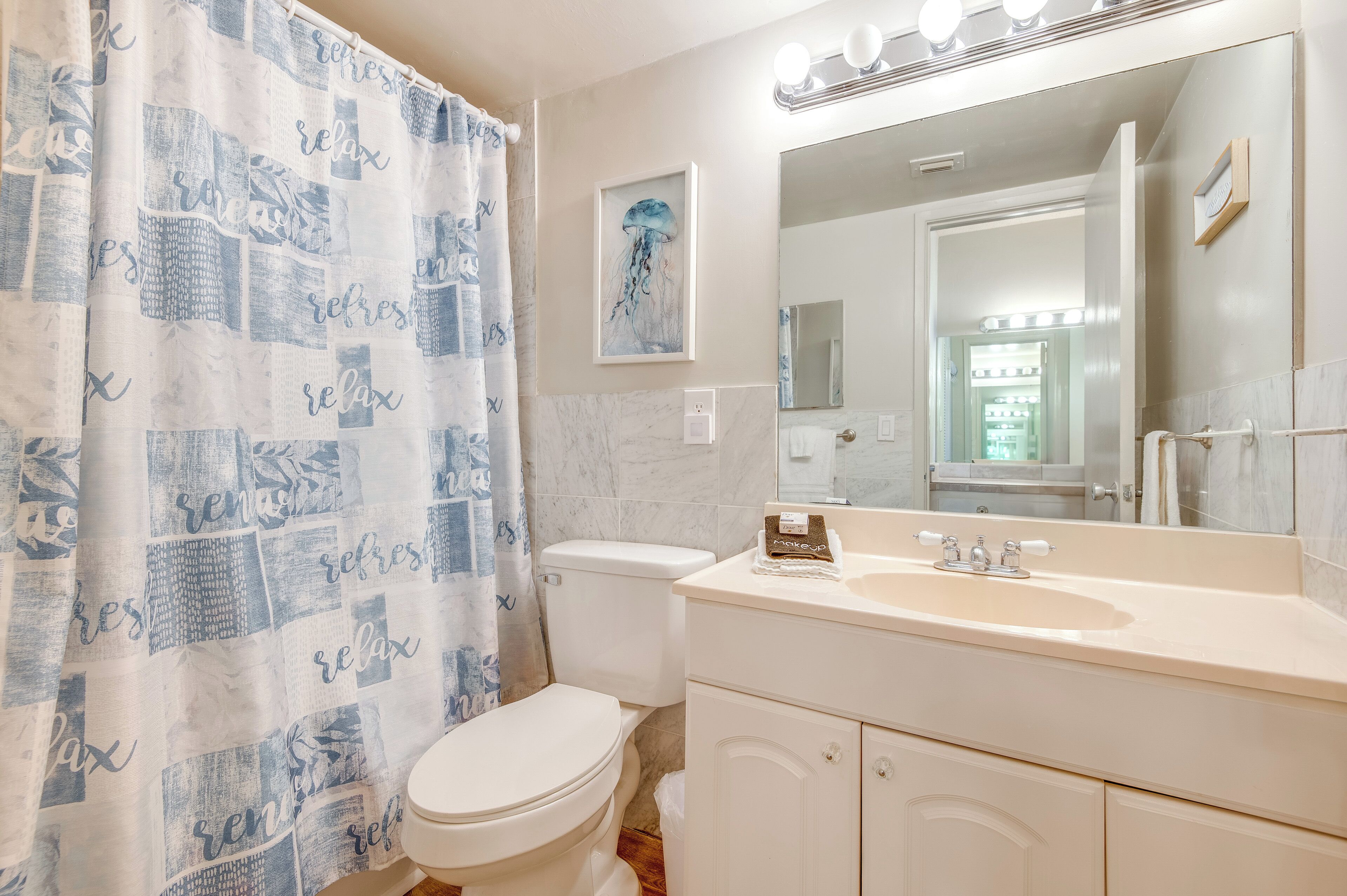 A bathroom with a white toilet, a sink with a mirror, and a shower curtain with a pattern.