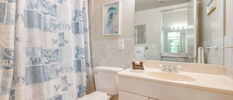A bathroom with a white toilet, a sink with a mirror, and a shower curtain with a pattern.