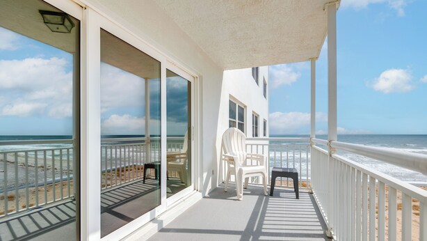 A balcony with a view of the beach, white chairs, and a table. - Direct Beach Access & View: Satellite Beach Condo! (Satellite Beach)