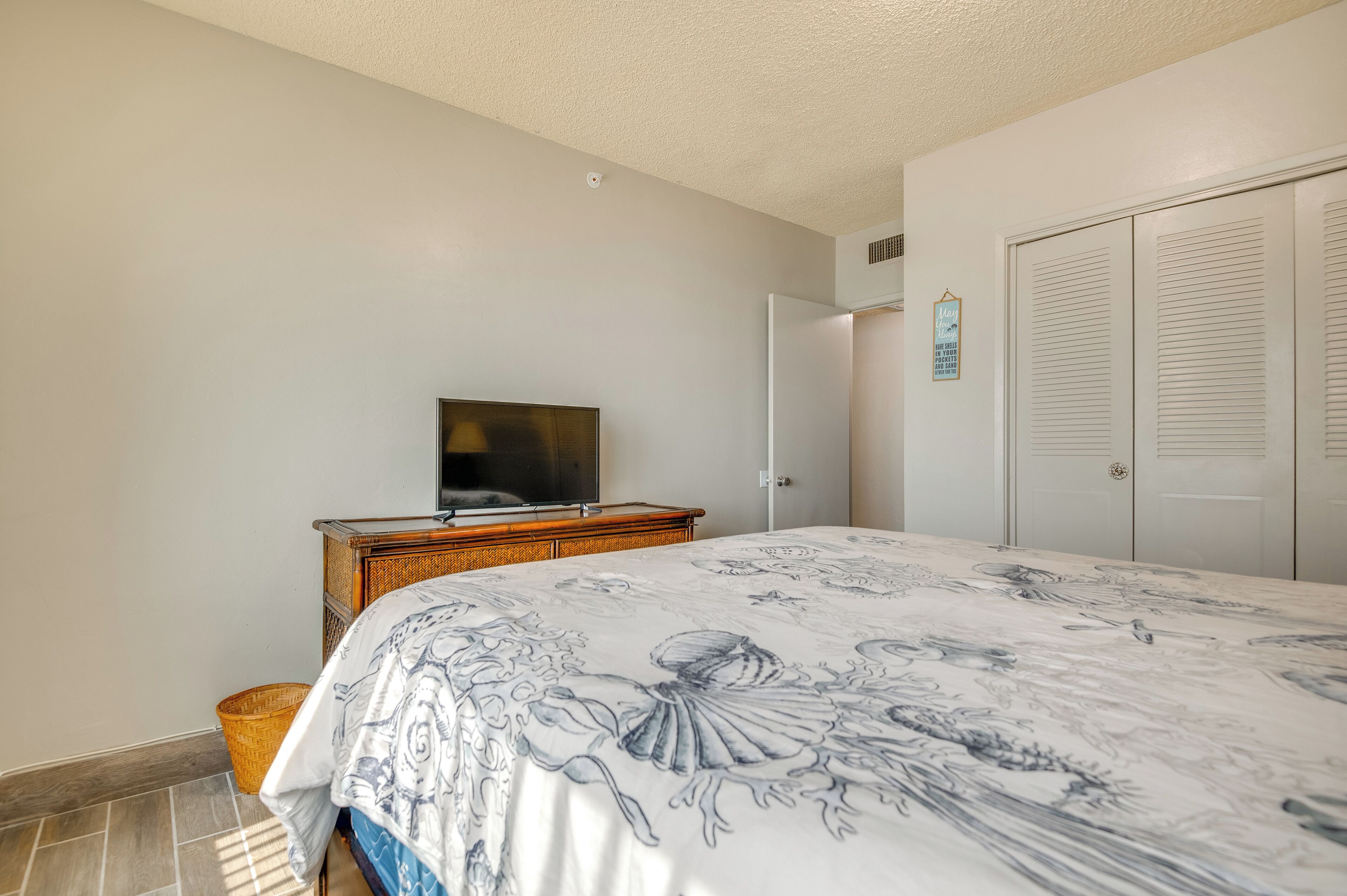 A bedroom with a bed, a television on a wooden dresser, a closet, and a small basket on the floor.