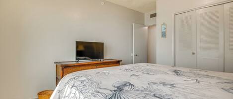 A bedroom with a bed, a television on a wooden dresser, a closet, and a small basket on the floor.