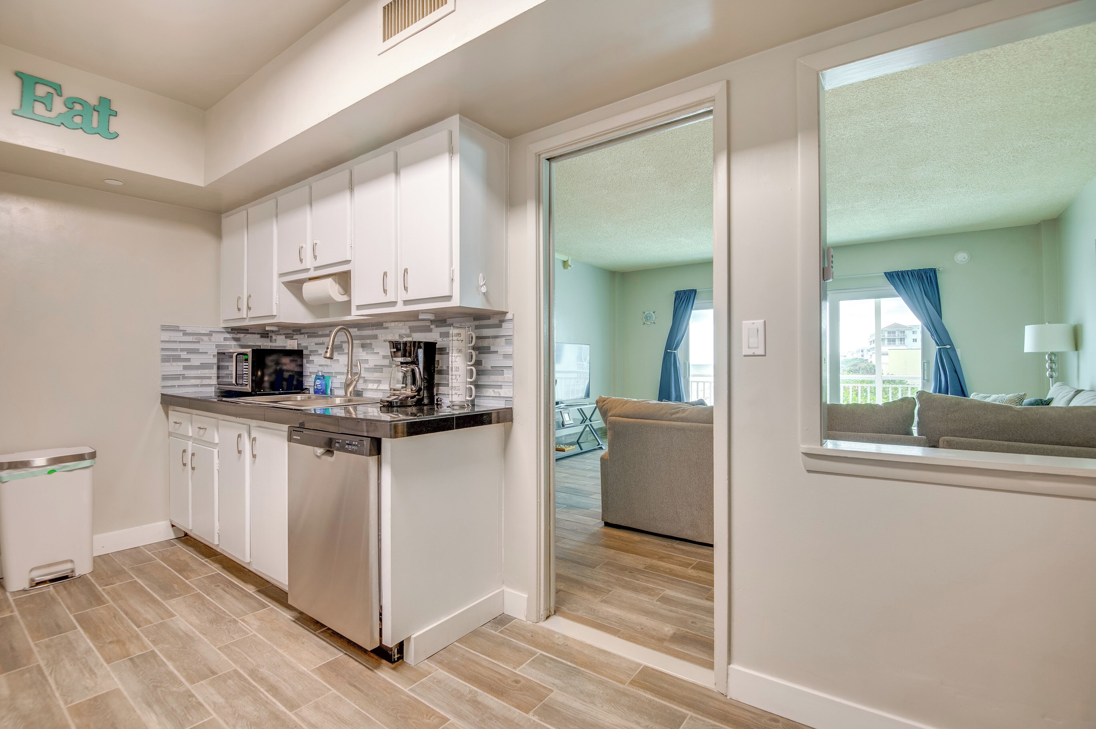 A modern kitchen with white cabinets, a dishwasher, and a countertop with a coffee maker.