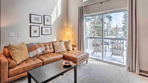 Ein Wohnzimmer mit braunem Ledersofa, einem Couchtisch und einem großen Fenster mit Blick auf Bäume und einen Balkon.