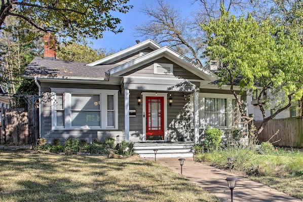 A single-story house with a red front door, a covered porch, and a small front yard with a pathway leading to the entrance.