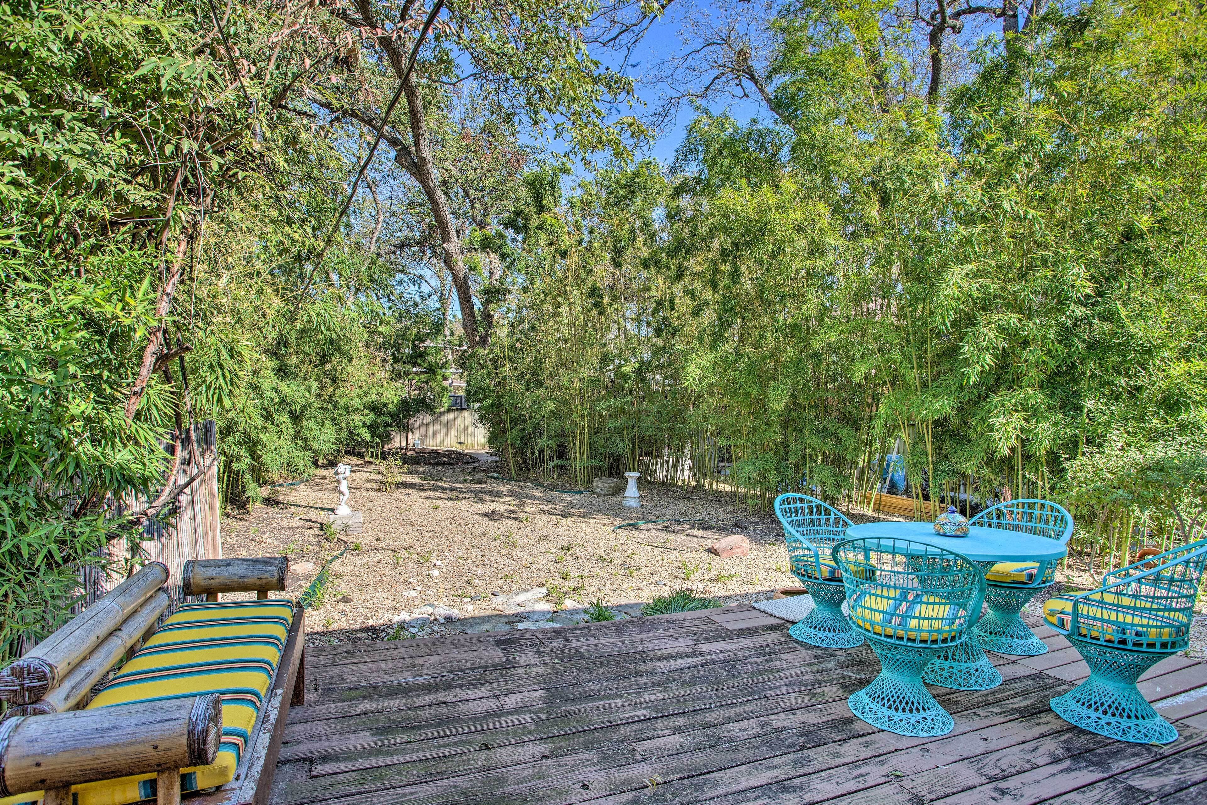 Une terrasse en bois, agrémentée de chaises turquoise et d’une table, entourée d’une végétation luxuriante et d’arbres.